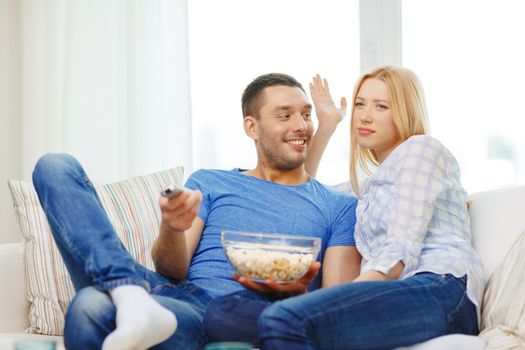 food, love, family and happiness concept - smiling couple with popcorn choosing what to watch at home