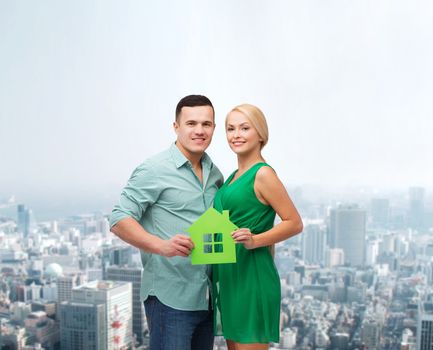 real estate, family and couple concept - smiling couple holding green paper house