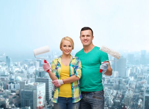 repair, construction and maintenance concept - smiling couple in gloves with paint rollers