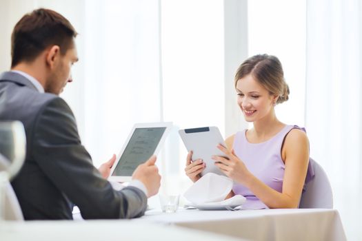 restaurant, couple, technology and holiday concept - smiling couple with menus on tablet pc computers at restaurant