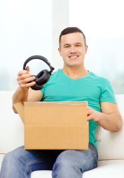 post, home, technology and lifestyle concept - smiling man opening cardboard box with headphones in it