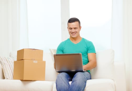 technology, home and lifestyle concept - smiling man with laptop and cardboard boxes at home