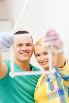 repair, building, family and home concept - smiling couple with house from measuring tape at home