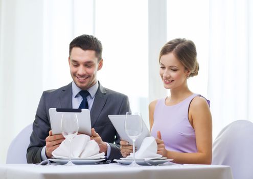 restaurant, couple, technology and holiday concept - smiling couple with menus on tablet pc computers at restaurant