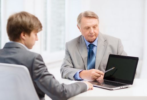 business, advertisement, technology and office concept - older man and young man with laptop computer in office