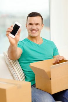 post, home, technology and lifestyle concept - smiling man opening cardboard box with smartphone in it