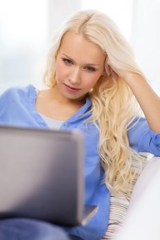 home, technology and internet concept - woman sitting on the couch with laptop computer at home