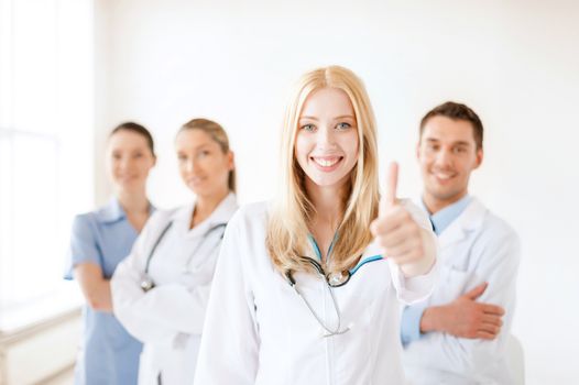 healthcare and medicine concept - attractive female doctor or nurse in front of medical group in hospital showint thumbs up