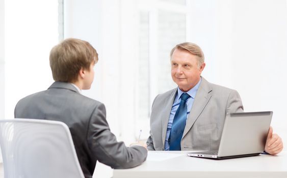 business, technology and office concept - older man and young man signing papers in office