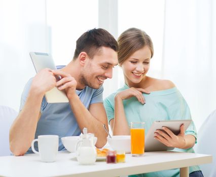 food, home, couple and technology concept - smiling couple with tablet pc reading news and having breakfast at home