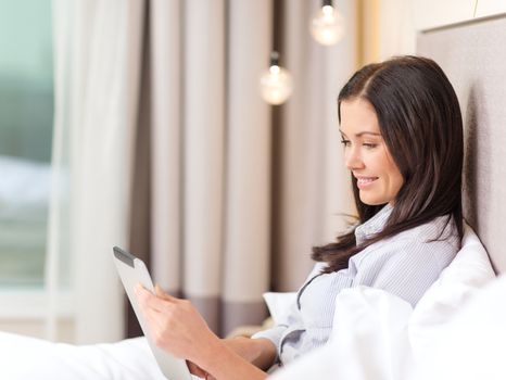 business, technology, internet and hotel concept - happy businesswoman with tablet pc computer lying in hotel in bed