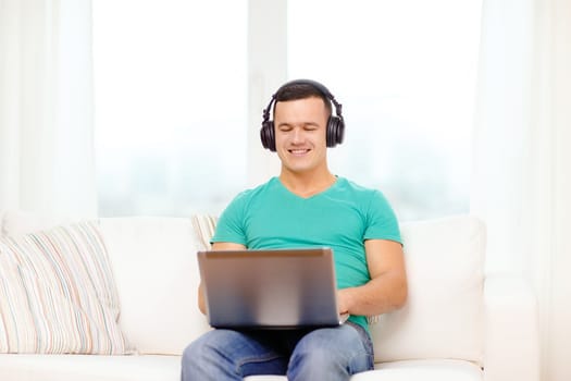 technology, home, music and lifestyle concept - smiling man with laptop and headphones at home