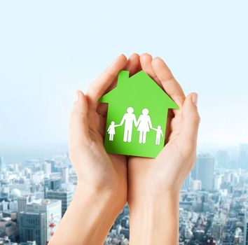 real estate and family home concept - closeup picture of female hands holding green paper house with family