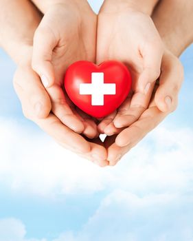 family health, charity and medicine concept - male and female hands holding red heart with cross sign