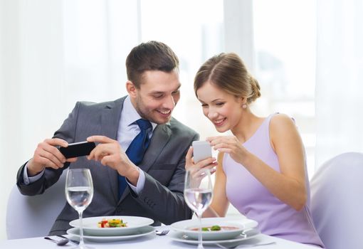 restaurant, couple, technology and holiday concept - smiling woman showing picture to husband or boyfriend on smartphone at restaurant