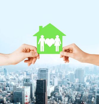 real estate and family home concept - isolated picture of male and female hands holding green paper house with family