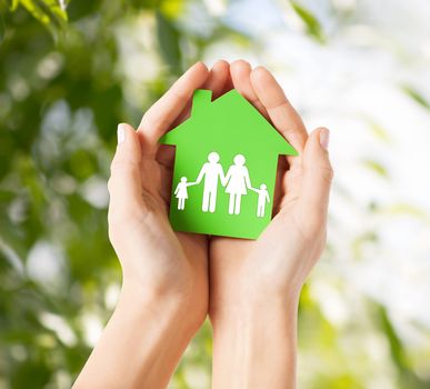 real estate and family home concept - closeup picture of female hands holding green paper house with family