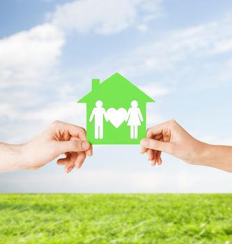 real estate and family home concept - isolated picture of male and female hands holding green paper house with family