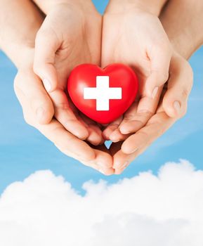 family health, charity and medicine concept - male and female hands holding red heart with cross sign