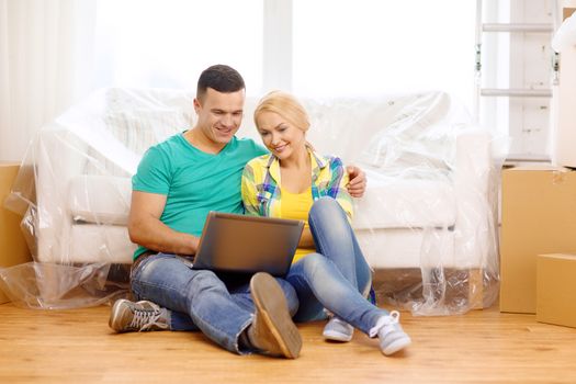 moving, home, technology and couple concept - smiling couple with laptop sitting on floor in new house