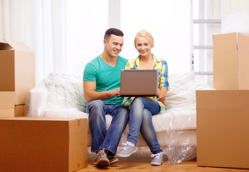 moving, home, technology and couple concept - smiling couple relaxing on sofa with laptop in new home