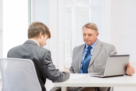 business, technology and office concept - older man and young man signing papers in office