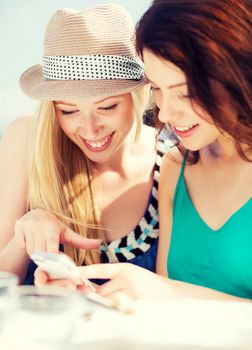 summer holidays, vacation and internet - girls looking at smartphone in cafe