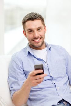 home, technology and internet concept - smiling man with smartphone sitting on couch at home