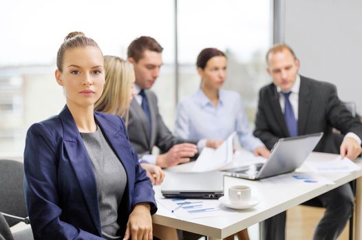 business, technology and office concept - smiling businesswoman in office with team on the back