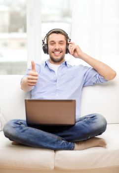 technology, home, music and lifestyle concept - smiling man with laptop and headphones at home showing thumbs up