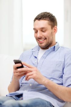 home, technology and internet concept - smiling man with smartphone sitting on couch at home