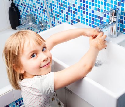 Little girl washing her hands in bathroom sink