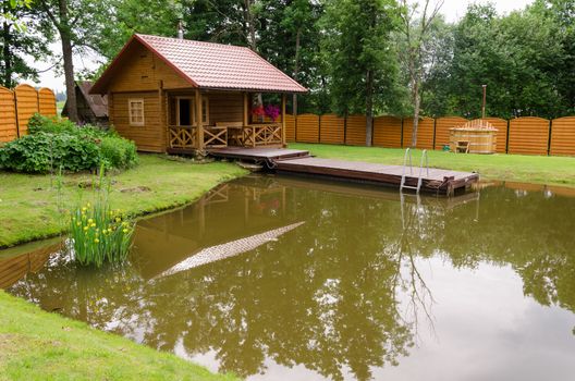 wooden new rural bathhouse and pond with floating plank footbridge in garden