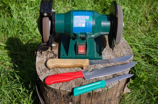 electric knife sharpening device and three kitchen knives on stump outdoor