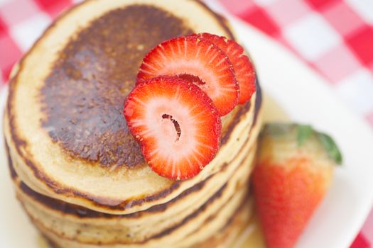 Pancakes, honey and strawberry on checkered fabric