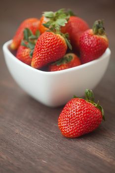 red juicy strawberry in a bowl on a wooden surface