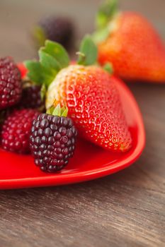 red juicy strawberry and blackberry in red plate on a wooden surface