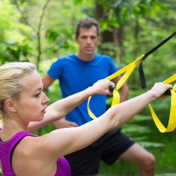 Young active people does suspension training with fitness straps outdoors in the nature.