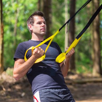 Young attractiveman does suspension training with fitness straps outdoors in the nature.