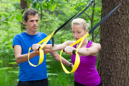 Young active people does suspension training with fitness straps outdoors in the nature.
