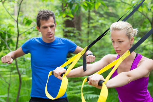 Young active people does suspension training with fitness straps outdoors in the nature.