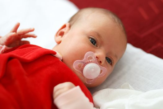 newborn, lying one month old baby in red dress with pacifier