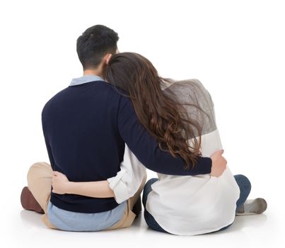 Asian couple sit on ground and hug each other, rear view on white background.