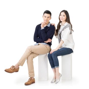 Attractive young Asian couple sit on boxes, full length portrait isolated on white background.