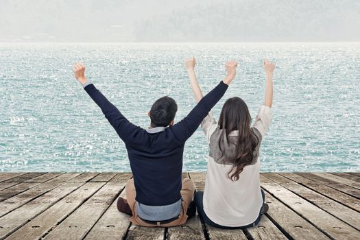 Asian couple sit on wooden ground and feel exciting against the lake with copyspace.