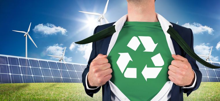 Businessman opening shirt in superhero style against large solar panel and three wind turbines