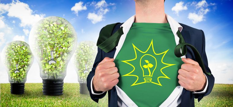 Businessman opening shirt in superhero style against three big light bulbs on the grass
