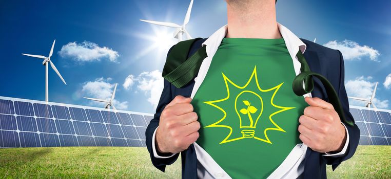 Businessman opening shirt in superhero style against large solar panel and three wind turbines