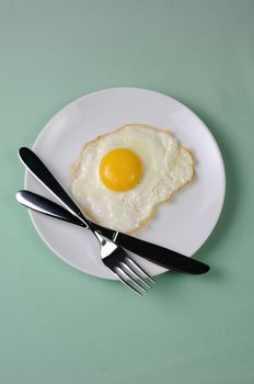 Fried eggs on a white plate with knife and fork