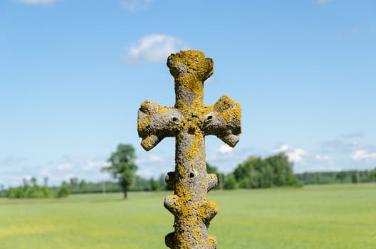 mossy old stone cross closeup on background of blue cloudy sky.
